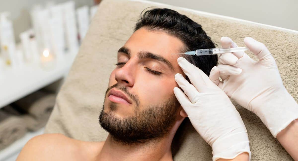a bearded man undergoing treatment with a needle prick on his forehead